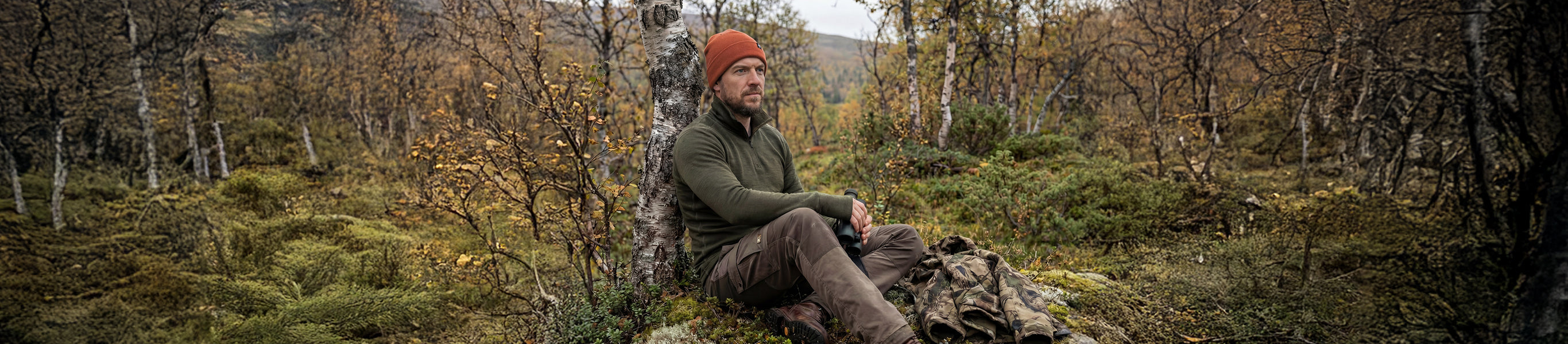 Green sweater flying on a grassy hill with mountains and clouds in the background