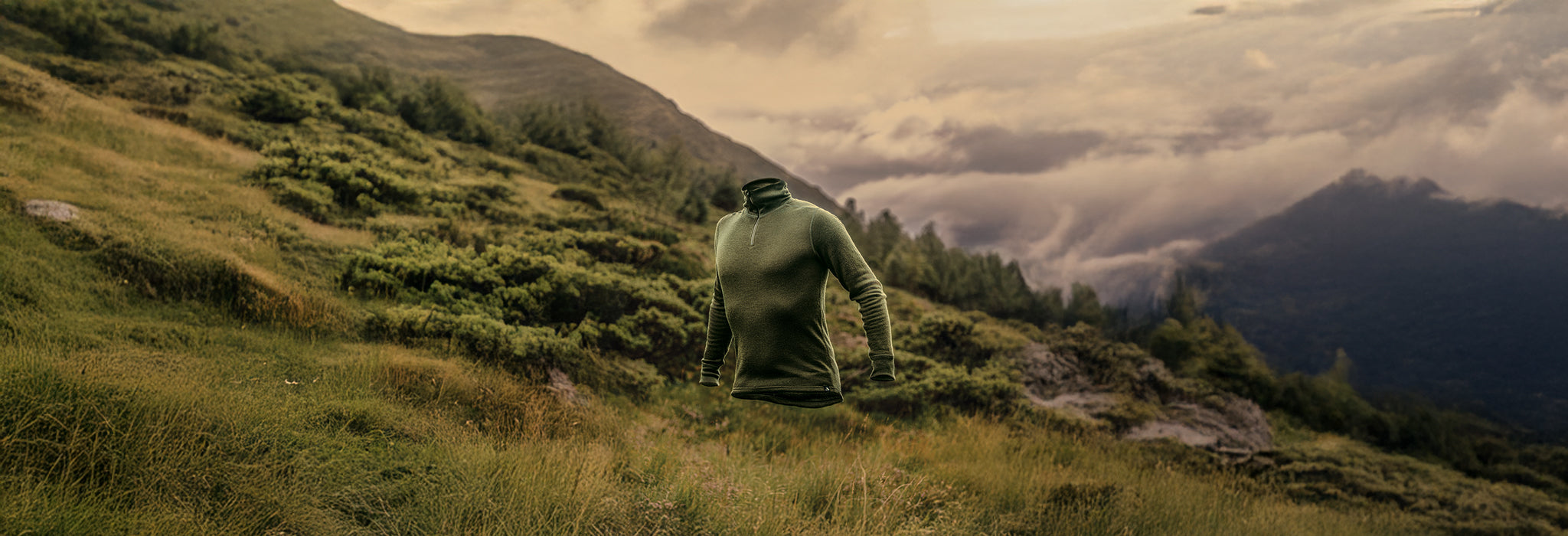 Green sweater flying on a grassy hill with mountains and clouds in the background