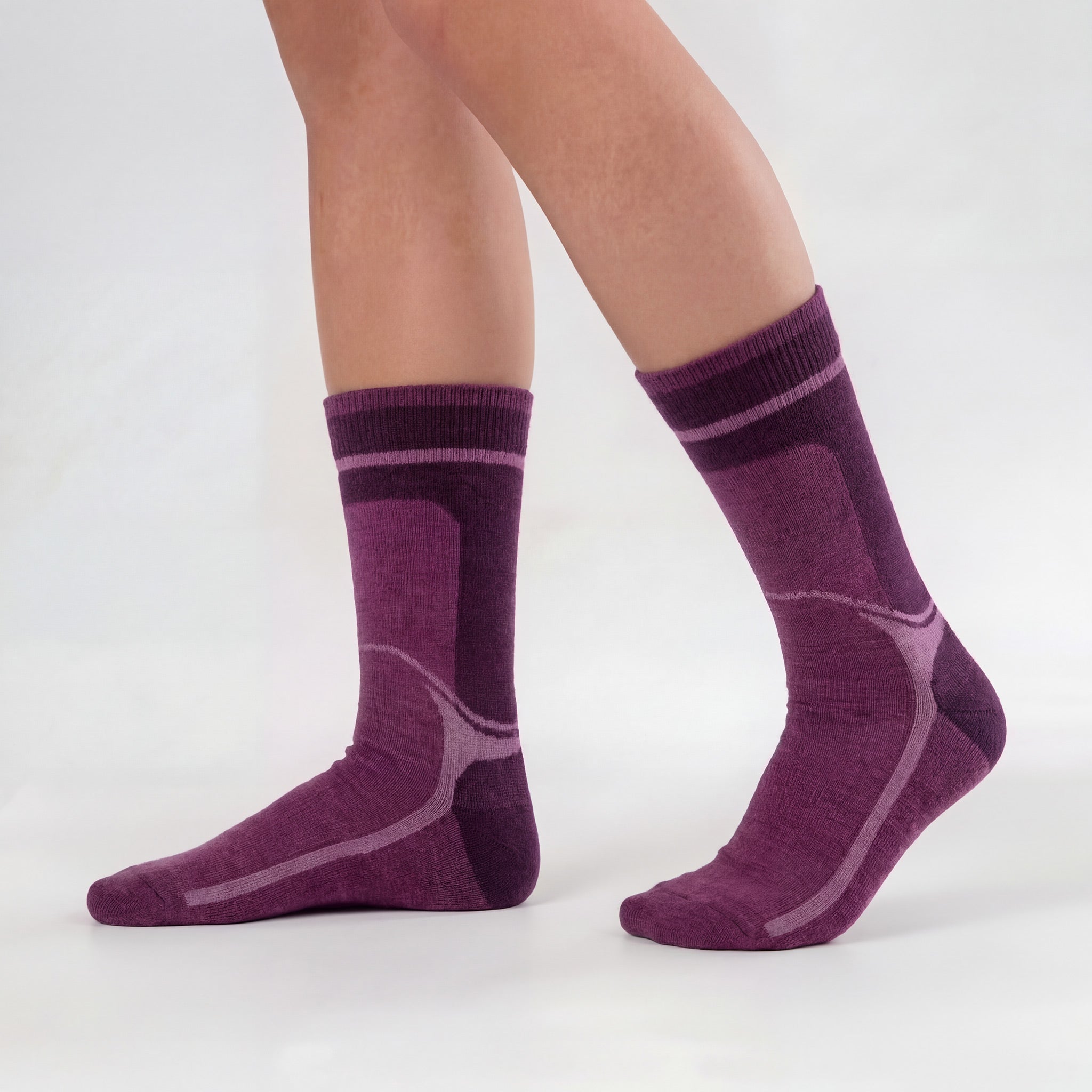 A person stands on a plain white background, showing a side view of both feet while wearing thick, comfortable Janusull wool socks in burgundy.