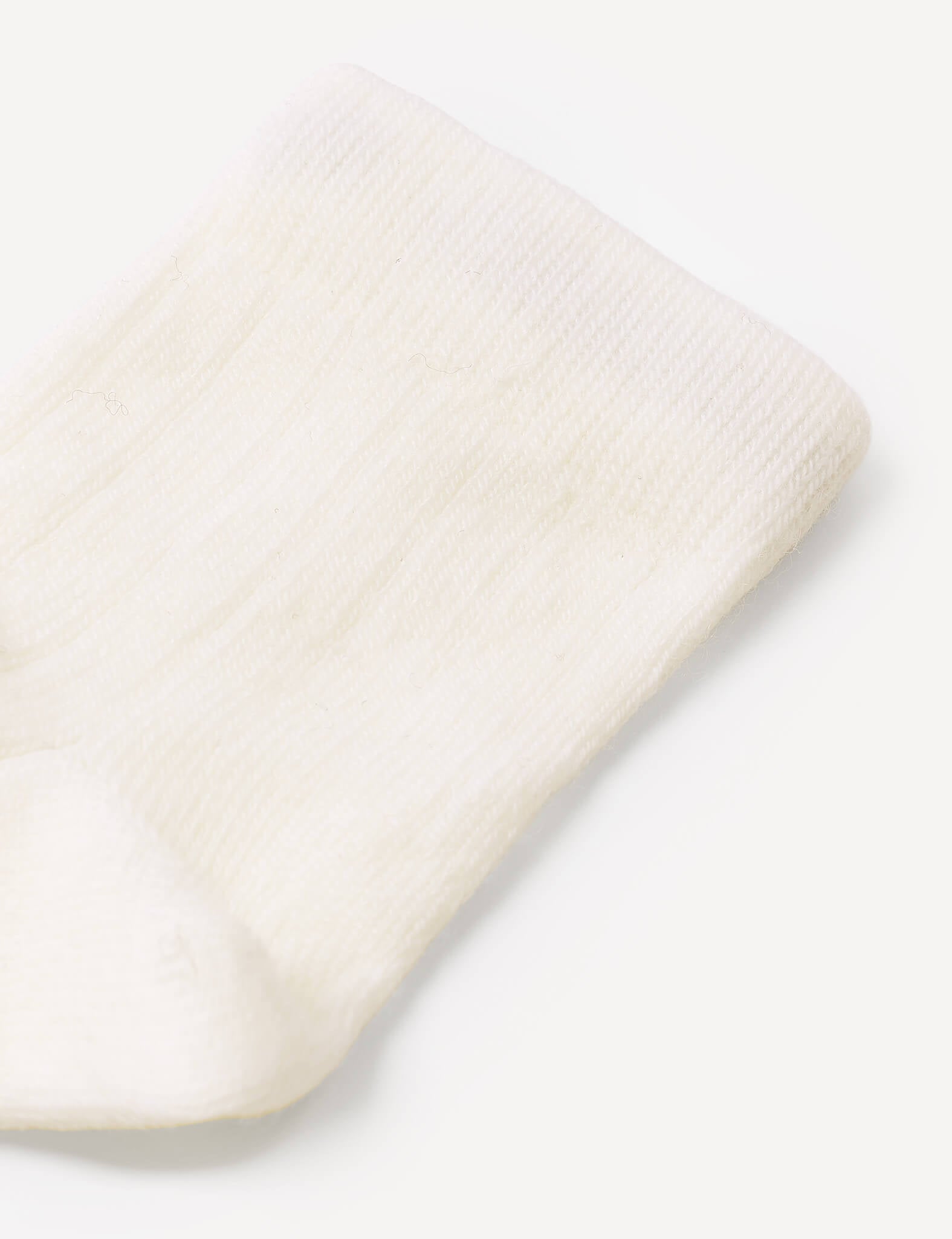 Close-up of a white, ribbed, knitted Socks – Merino Baby Light on a light background. The texture and pattern of the fabric are clearly visible, highlighting the quality craftsmanship and durability of these baby socks.