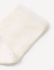 Close-up of a white, ribbed, knitted Socks – Merino Baby Light on a light background. The texture and pattern of the fabric are clearly visible, highlighting the quality craftsmanship and durability of these baby socks.