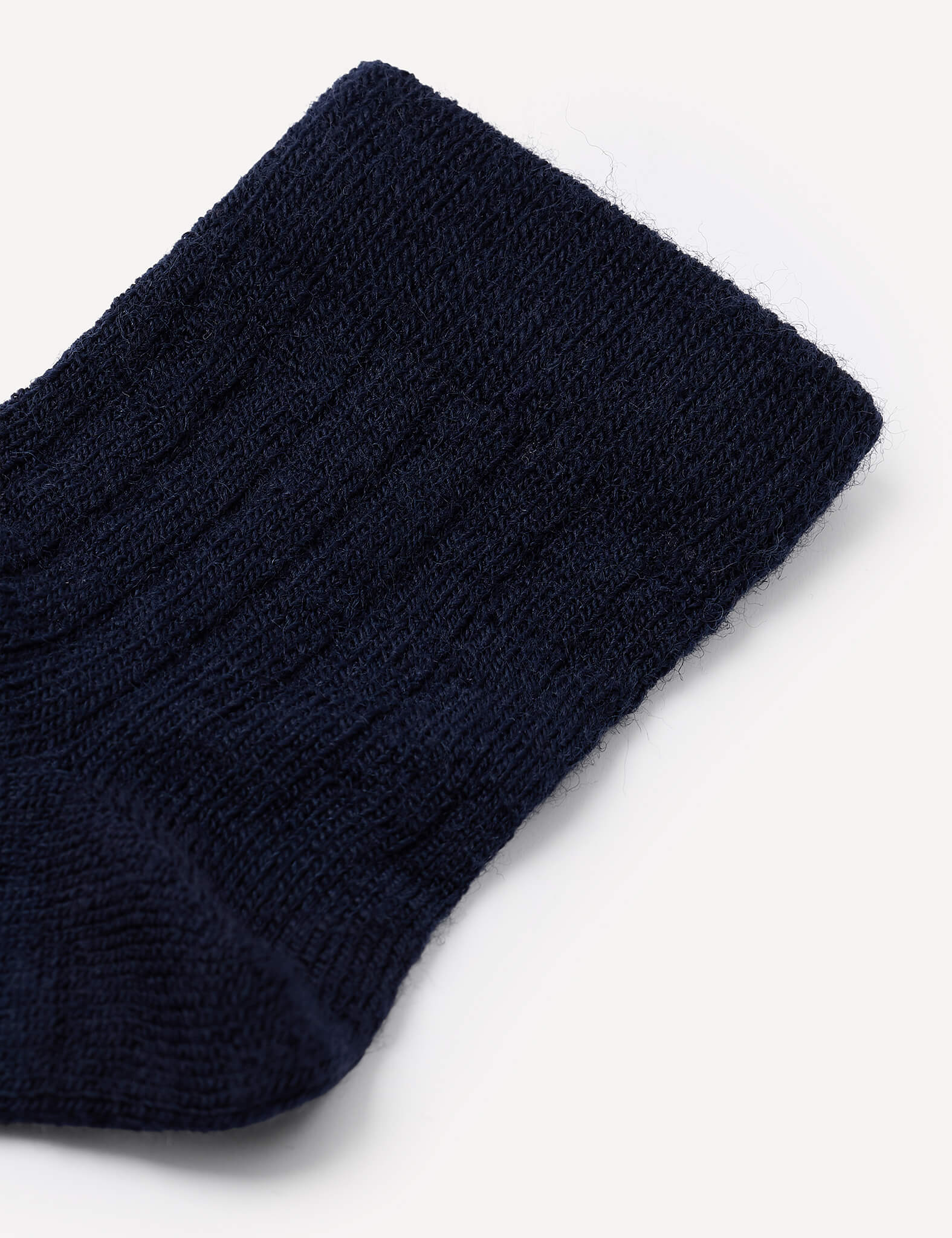 Close-up of the upper portion of a navy blue knit sock, showing its ribbed texture and cuff on a plain white background. This image showcases the design characteristic of the Socks – Merino Baby Light.
