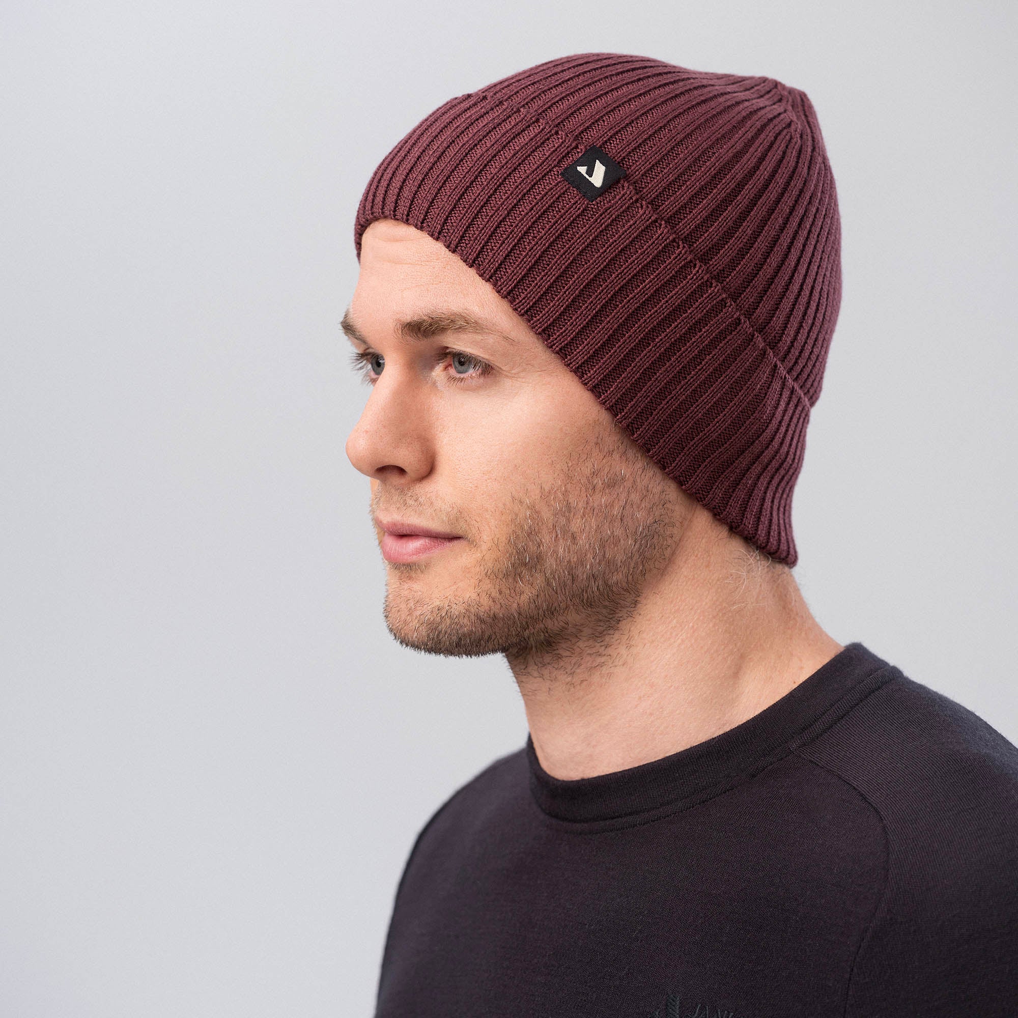 A man wears the Classic Beanie in maroon and a black crewneck shirt, looking to the side against a plain light gray background, highlighting the beanie’s warmth and breathability.