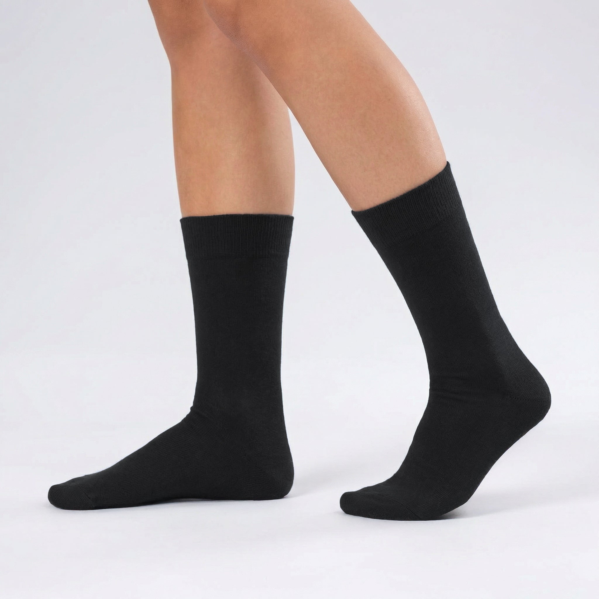 Someone is wearing Socks 3-pack – Daily Light in black, standing on a white surface with one foot slightly forward. The background is light gray.
