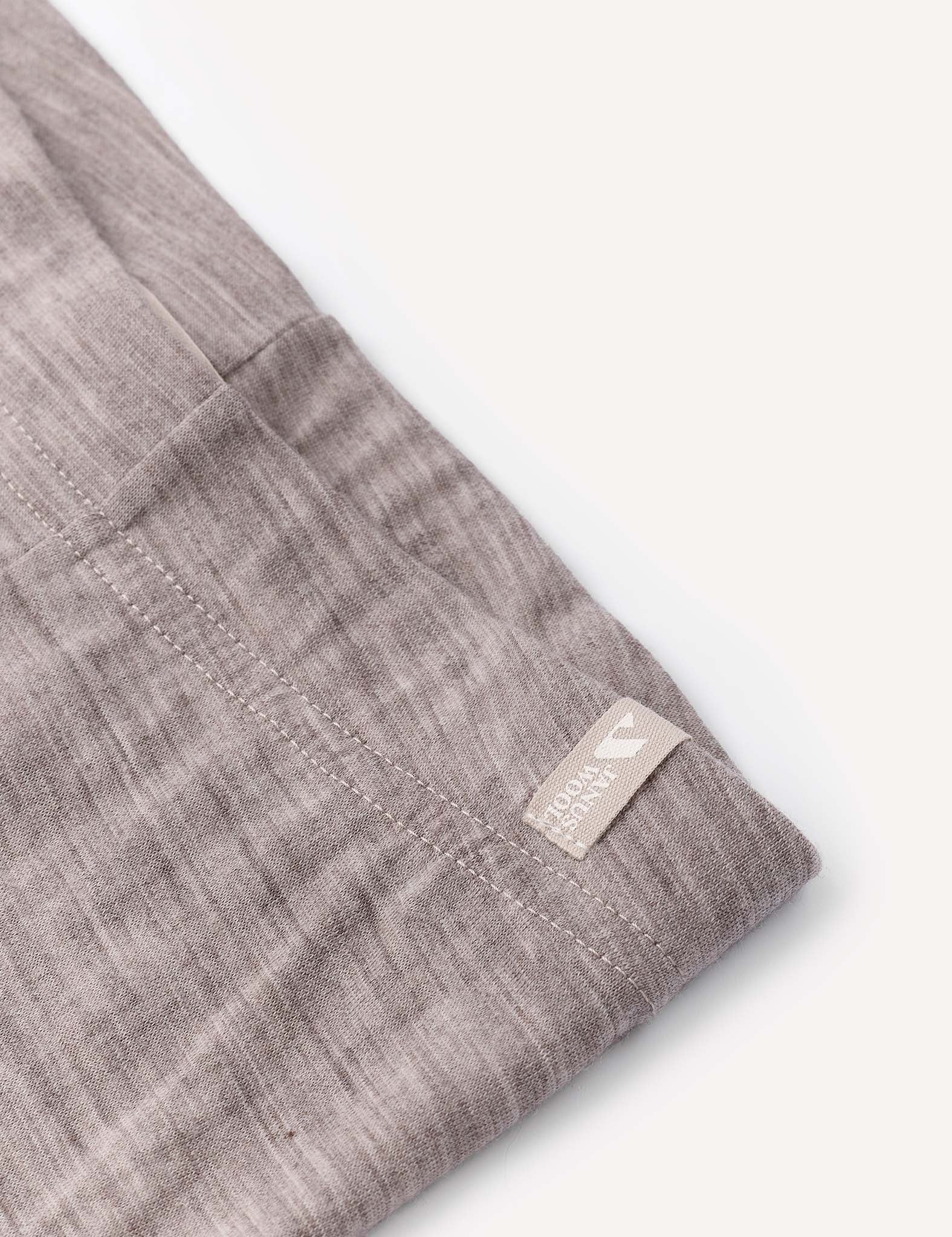 A close-up of a light brown, textured fabric with visible stitching and a small beige tag reading 100% linen attached to the edge—perfect for wearing as a comfortable base layer beneath the Leggings – Merino Baby Light.