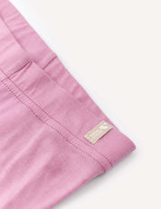 Close-up of a light pink fabric with visible stitching and a beige tag labeled 100% TENCEL™ LYOCELL stitched on the edge, set against a plain, light background—perfect as the soft base layer offered by our Leggings – Merino Baby Light for added comfort.