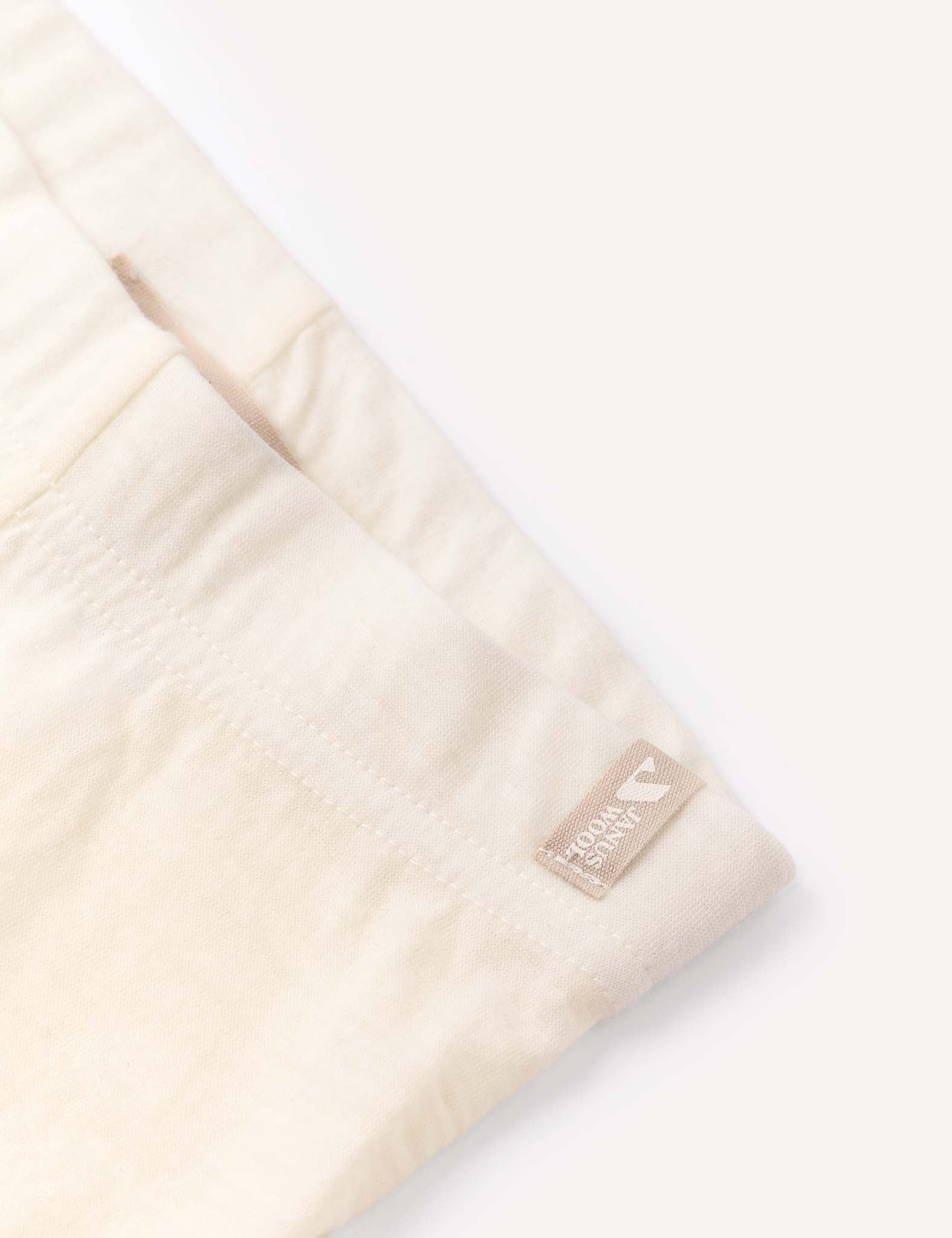 Close-up of a light beige, soft fabric garment identified as the Leggings – Merino Baby Light, featuring a small tan woven label reading 100% TENCEL LYOCELL sewn into the seam. This fabric is ideal for use as a base layer or lightweight leggings. The background is a plain, light color.