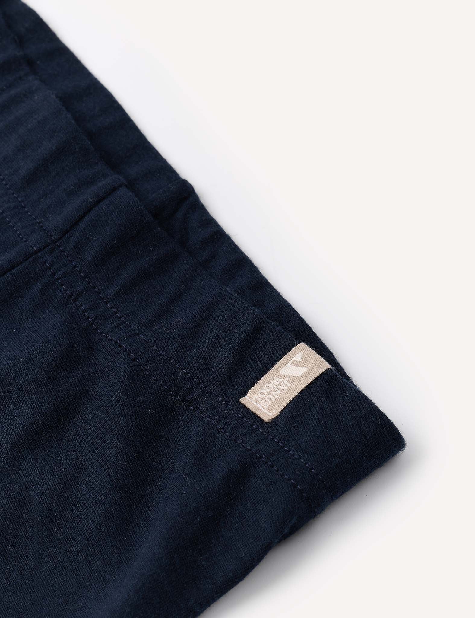 Close-up of the Leggings – Merino Baby Light in navy blue, featuring a beige tag with small text and a heart icon sewn into the seam. This merino fabric is perfect for base layers or lightweight leggings. The background is a light, neutral tone.