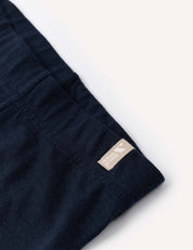 Close-up of the Leggings – Merino Baby Light in navy blue, featuring a beige tag with small text and a heart icon sewn into the seam. This merino fabric is perfect for base layers or lightweight leggings. The background is a light, neutral tone.