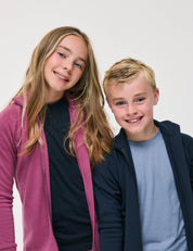 Two smiling children, a girl in a pink hoodie and a boy in a navy hoodie layered over the T-Shirt – Merino Kids Light in light blue, stand close together against a plain white background, showcasing all-day comfort and excellent temperature regulation.