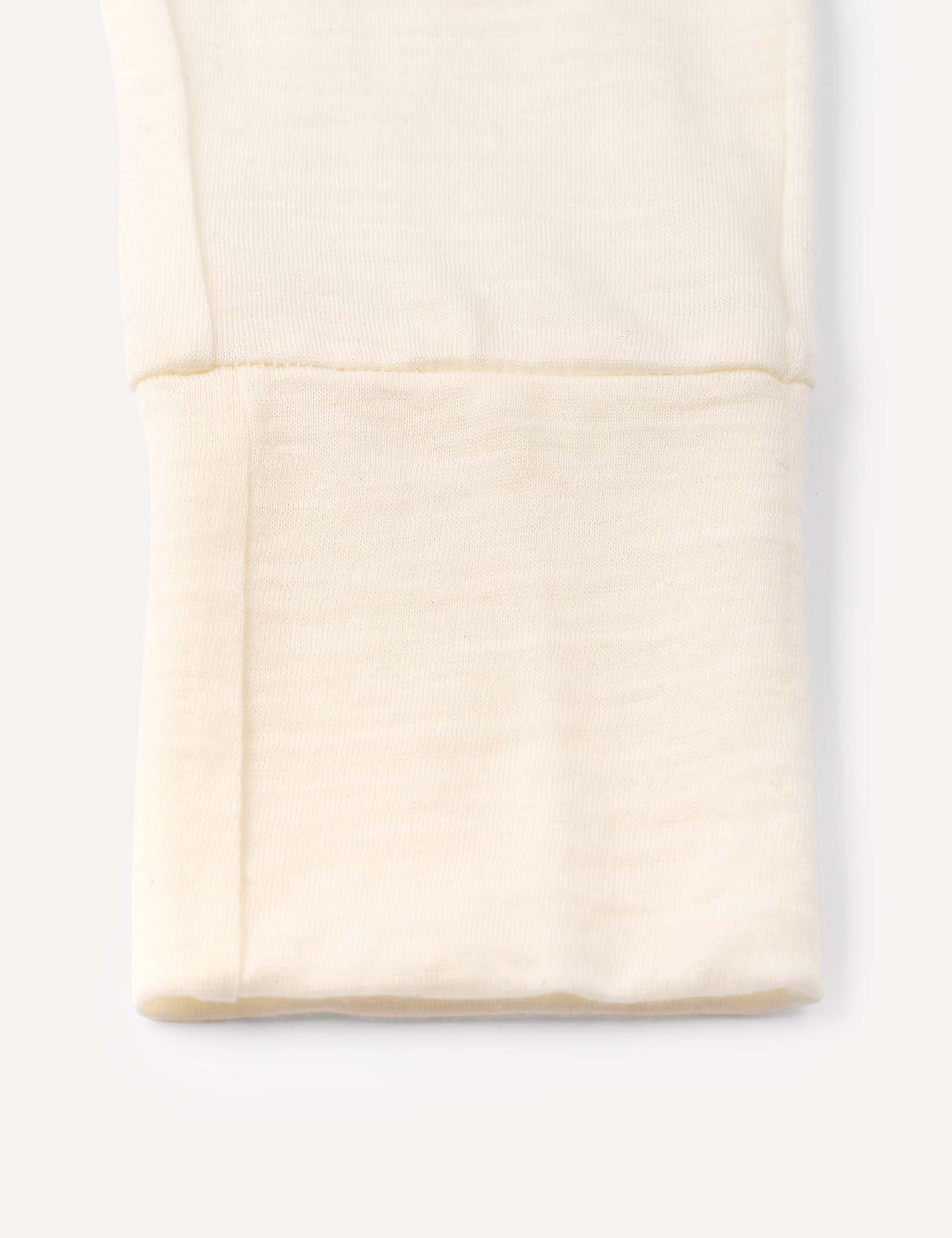 A close-up of a folded, cream-colored Merino Baby Light pyjamas fabric with a visible seam, possibly showing the cuff of a long sleeve top or pants, made from breathable material and displayed against a plain white background.