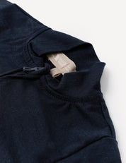 Close-up of the Pyjamas – Merino Baby Light in navy blue, featuring a standing collar with an exposed zipper and a beige tag with red text at the neckline, laid on a white surface. Crafted from breathable merino nightwear material designed for superior comfort.