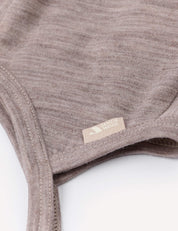 Close-up of the Bonnet – Merino Baby Light, crafted from soft, light brown merino wool. A small beige tag with a subtle logo and text is stitched near the seam, highlighting the fabric’s fine texture and neat stitching.