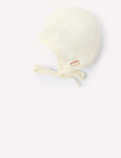 Bonnet – Merino Baby Light in off-white featuring a lightweight chin tie and a small red and white side tag, displayed on a plain light background.