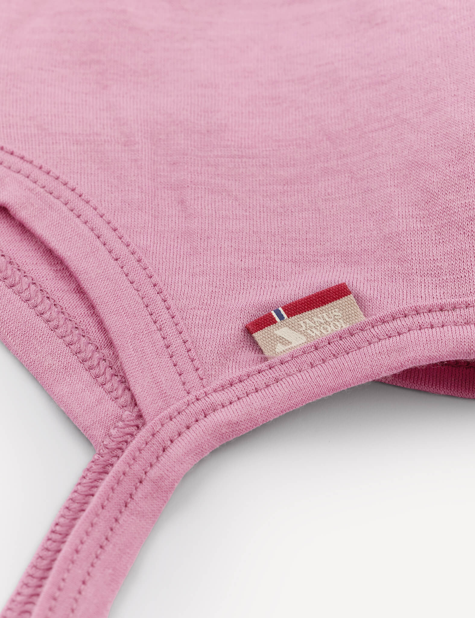 Close-up of a pink Bonnet – Merino Baby Light with visible stitching and a small beige tag featuring a red, white, and blue stripe detail. This breathable baby hat is designed for comfort and style.