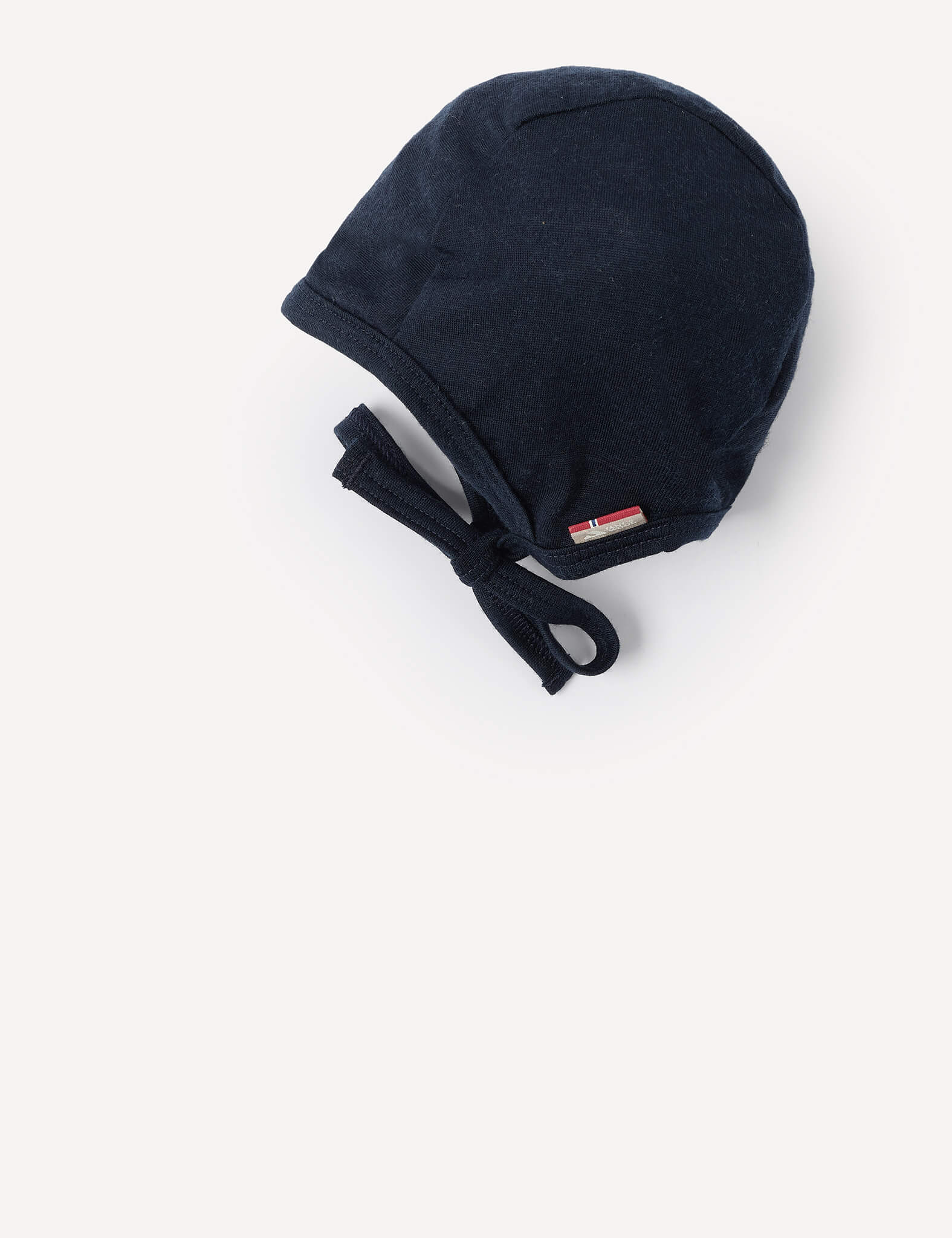 A Merino Baby Light bonnet in dark blue, featuring lightweight fabric and chin ties, is displayed lying flat on a white background.