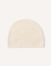 The Beanie – Merino Baby Light, in a simple light beige shade, features a rounded top and a fold-over brim. It is displayed flat against a white background, highlighting its breathable design.
