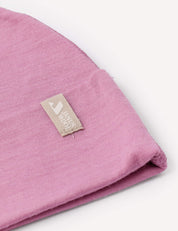 A close-up of a folded pink Beanie – Merino Baby Light hat features a beige label sewn on, displaying a white house icon and the words HOUSE HOOD.
