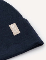 A close-up of the Beanie – Merino Baby Light in dark blue, featuring a beige fabric tag with “Hands Tools” in white text, displayed against a plain, light background.