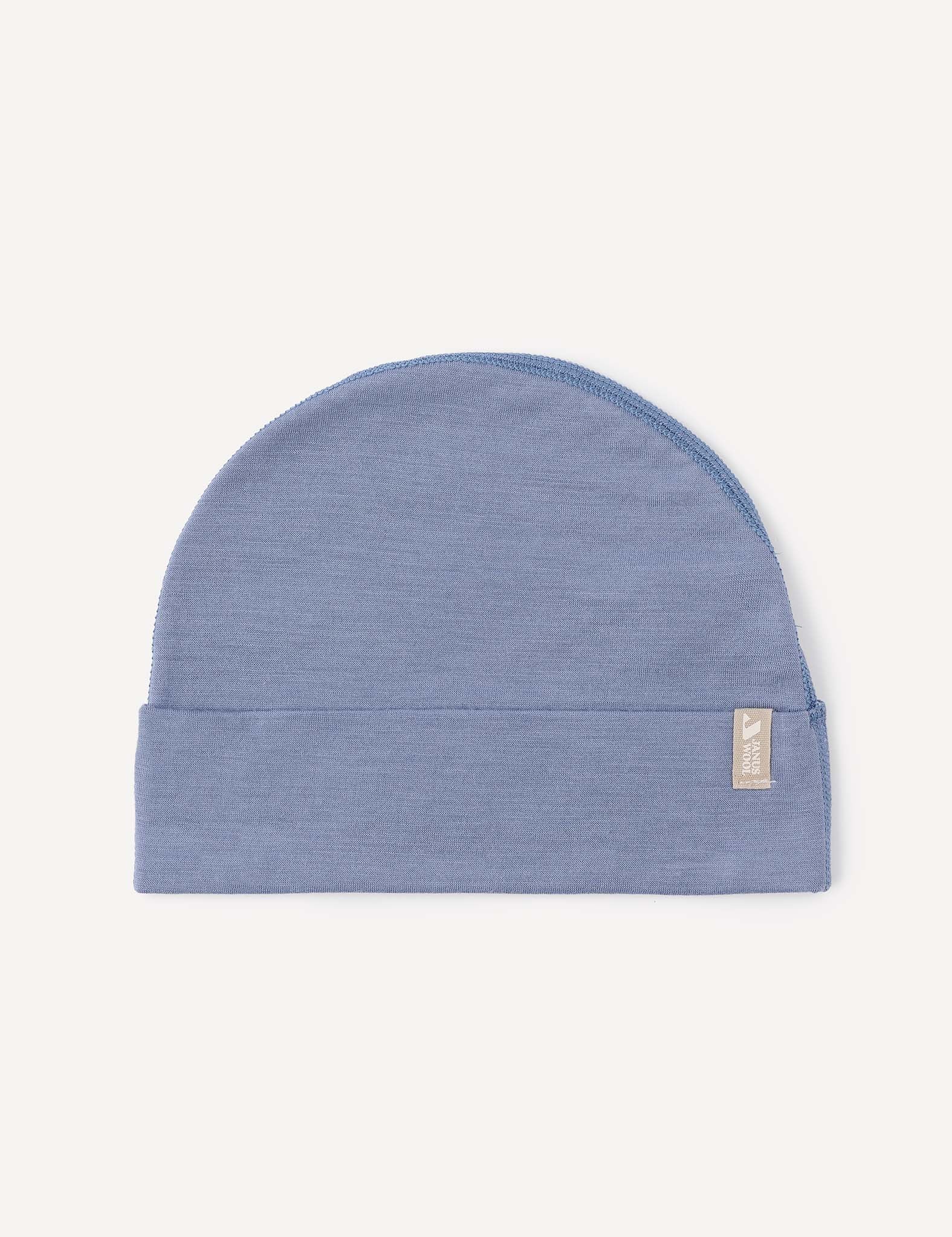 A lightweight “Beanie – Merino Baby Light” in Troposphere blue knit, featuring a folded brim and a small rectangular beige tag on the side, displayed against a plain off-white background.