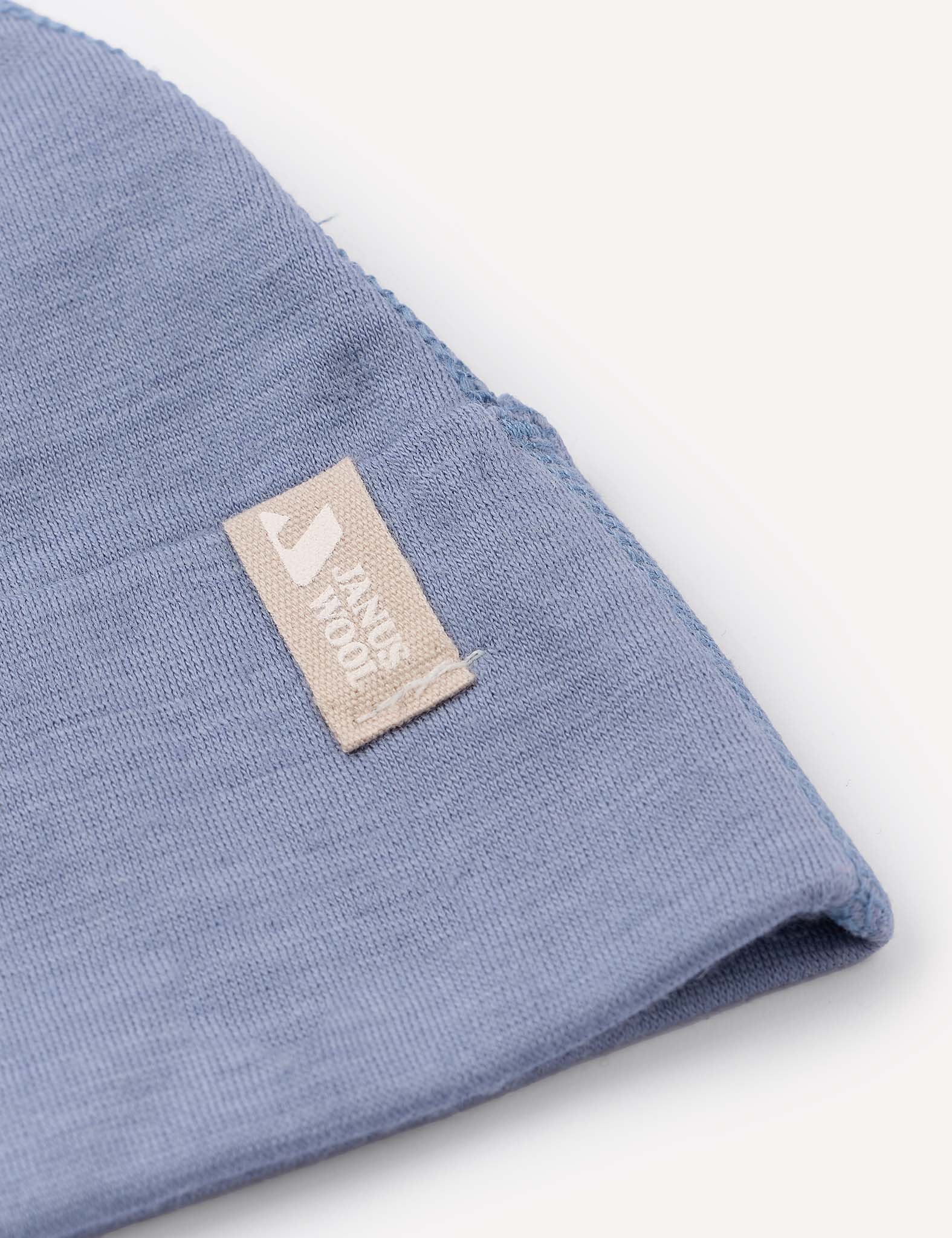 A close-up of a corner of the Beanie – Merino Baby Light in light blue, featuring a beige tag sewn on with the text HAND MADE and a small graphic.
