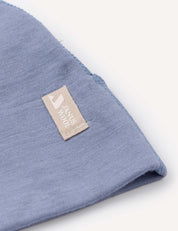 A close-up of a corner of the Beanie – Merino Baby Light in light blue, featuring a beige tag sewn on with the text HAND MADE and a small graphic.