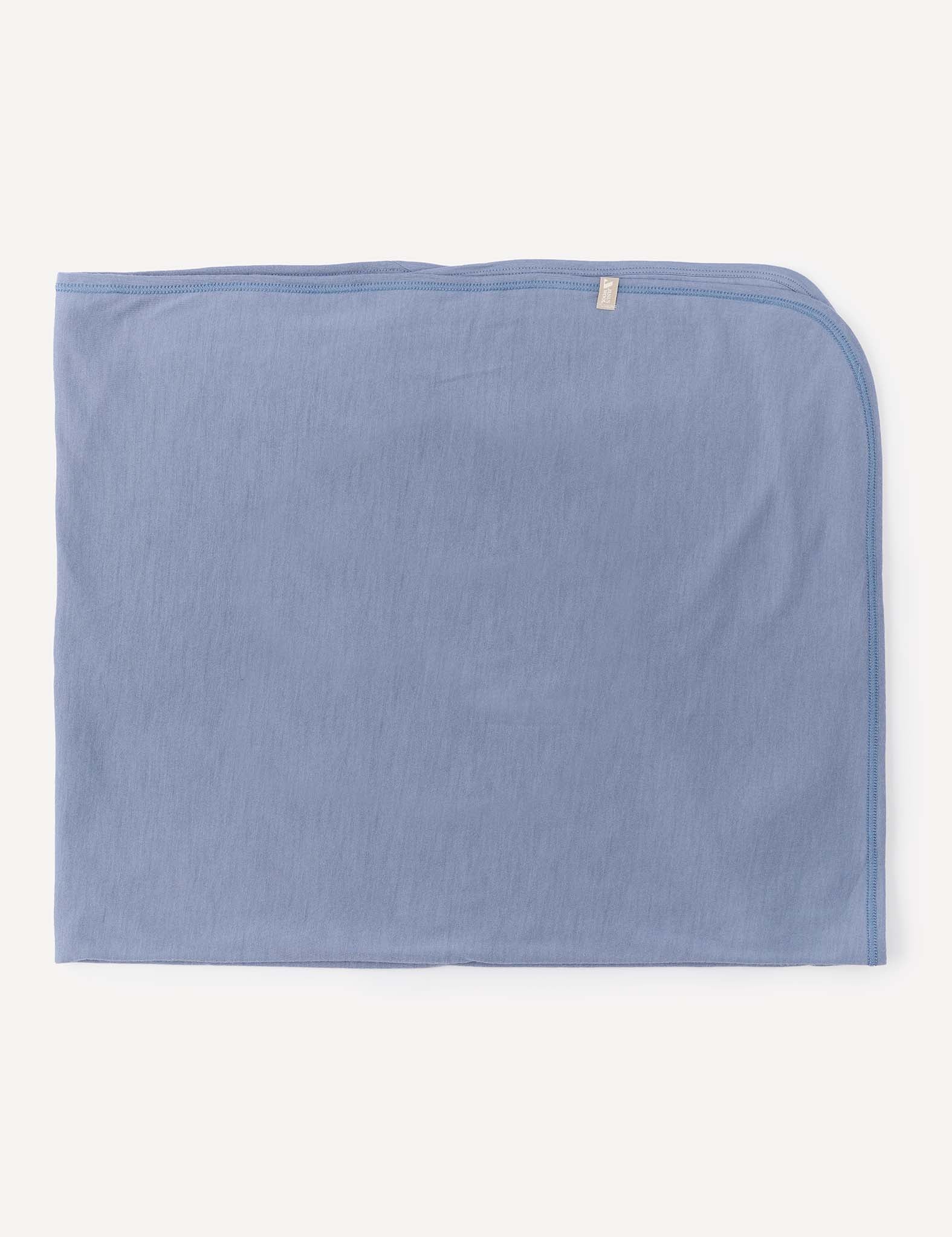 A Blanket – Merino Baby Light in light blue, lightweight and neatly folded with a small beige tag on one edge, displayed on a plain off-white background.