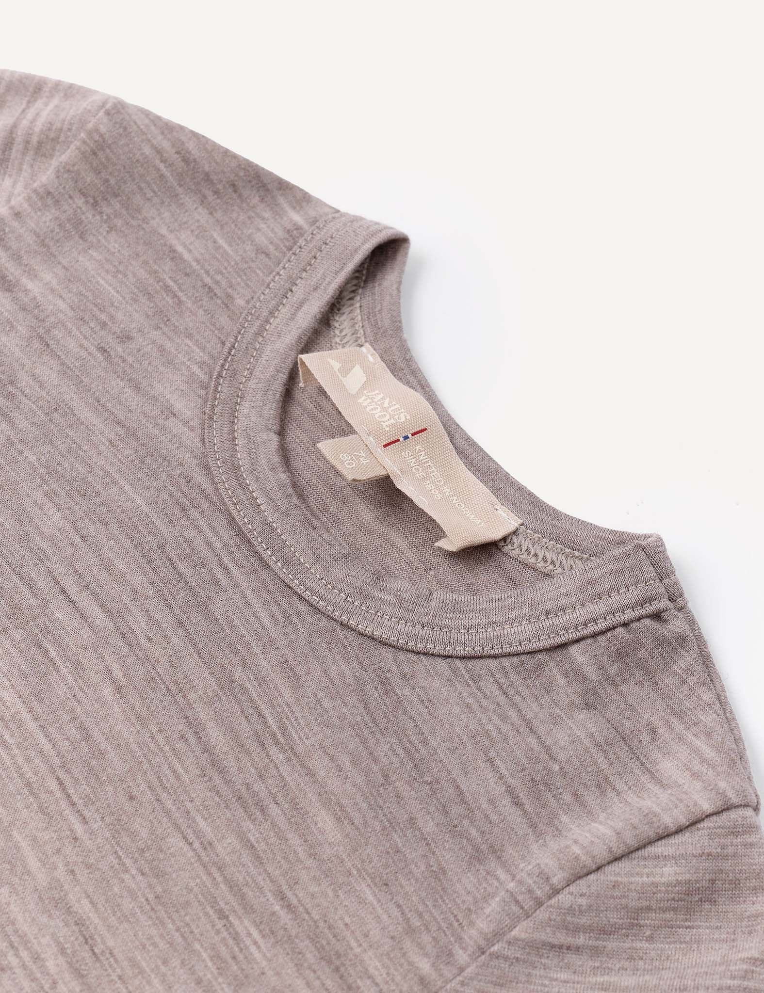 A close-up of the Body – Merino Baby Light, a light brown heathered crew-neck baby bodysuit featuring two beige clothing tags sewn into the collar, displayed on a white background. This breathable piece is perfect for comfort and style.