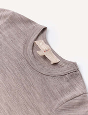 A close-up of the Body – Merino Baby Light, a light brown heathered crew-neck baby bodysuit featuring two beige clothing tags sewn into the collar, displayed on a white background. This breathable piece is perfect for comfort and style.