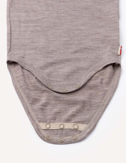 A close-up of the Body – Merino Baby Light in beige, highlighting the bottom snap buttons for easy diaper changes, laid flat on a white background.