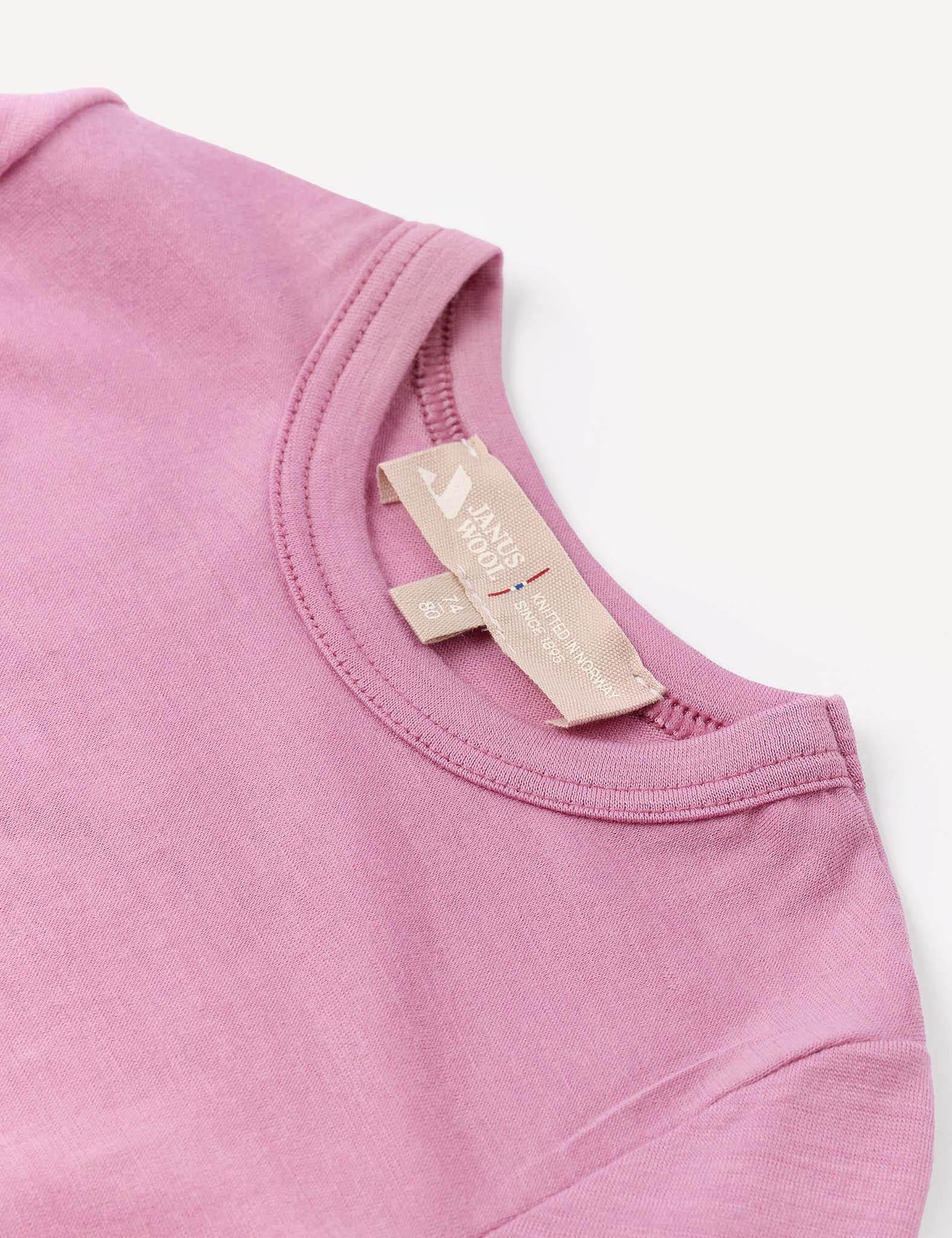 A close-up of the collar and beige fabric tags of the Body – Merino Baby Light, a light purple baby bodysuit, displayed on a white background.