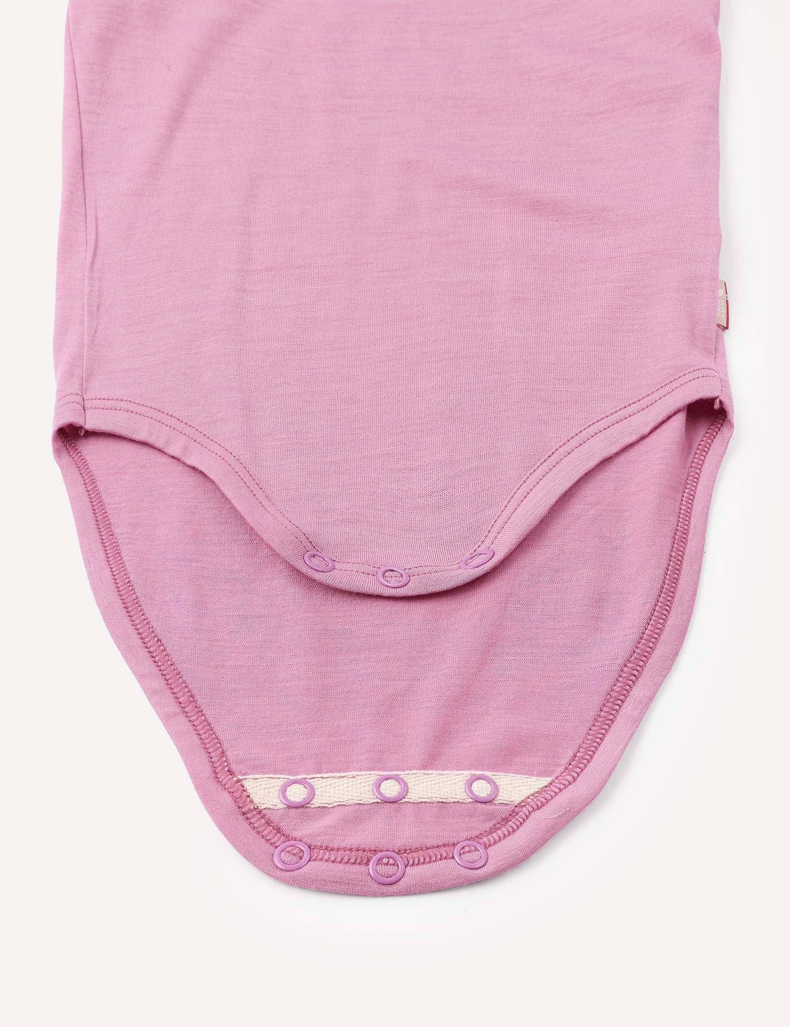 A close-up of the Body – Merino Baby Light in light purple shows the bottom with snap button closures open, revealing the soft merino inner fabric. This breathable baby bodysuit offers comfort and practicality for little ones.