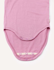 A close-up of the Body – Merino Baby Light in light purple shows the bottom with snap button closures open, revealing the soft merino inner fabric. This breathable baby bodysuit offers comfort and practicality for little ones.