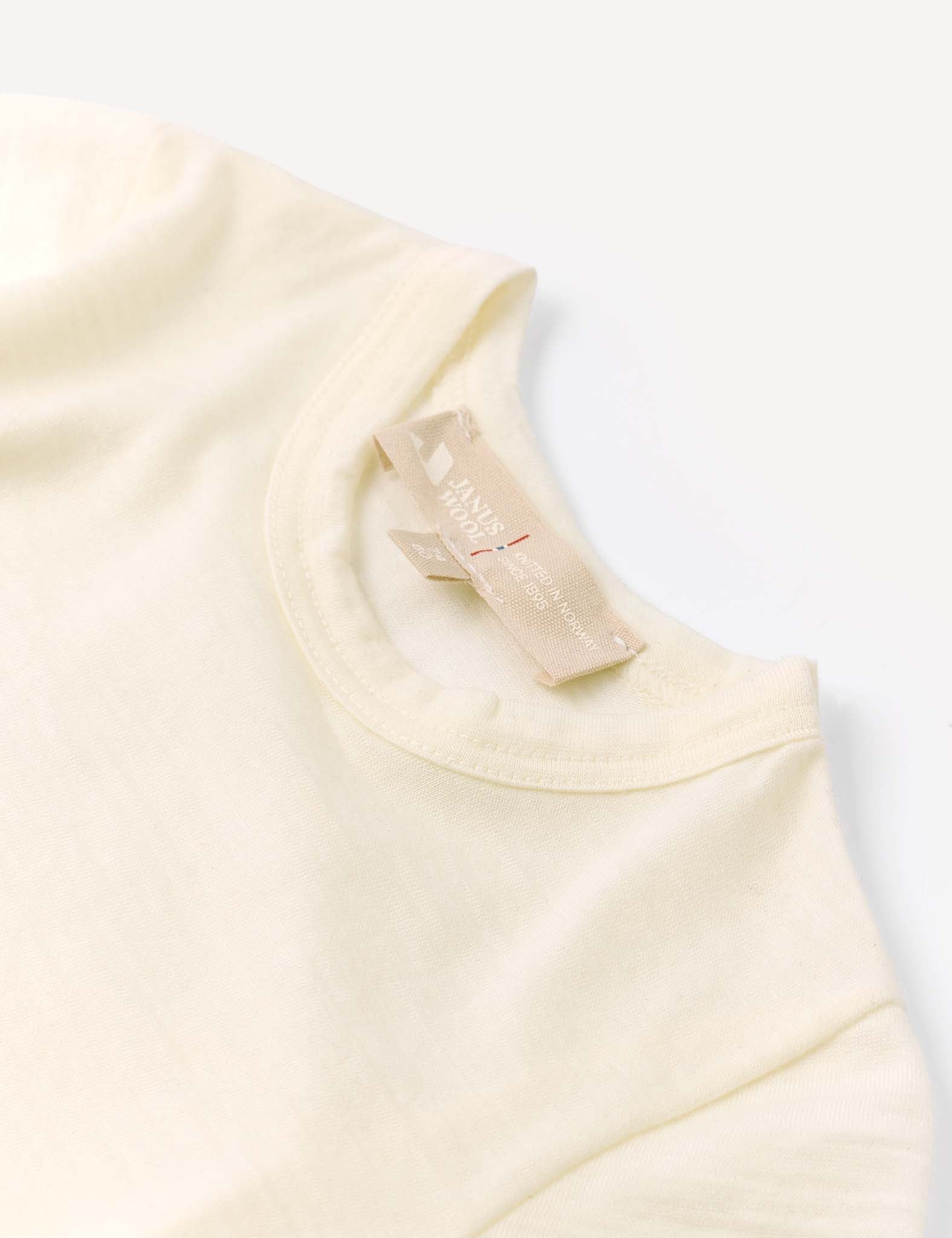 A close-up of the Body – Merino Baby Light’s cream-colored neckline and collar displays a beige fabric tag featuring HANIN text. This piece exemplifies breathable baby clothing, laid flat on a white surface.