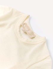A close-up of the Body – Merino Baby Light’s cream-colored neckline and collar displays a beige fabric tag featuring HANIN text. This piece exemplifies breathable baby clothing, laid flat on a white surface.