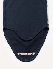 A close-up of the Body – Merino Baby Light, a dark merino wool baby bodysuit featuring snap buttons along two overlapping flaps, laid flat on a white background.