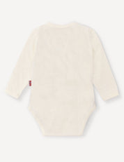 A back view of the Wrapover Bodysuit – Merino Baby Light is shown, highlighting its long sleeves and off-white color. The left side seam features a small tag, and the soft, breathable fabric suggests comfort for babies.