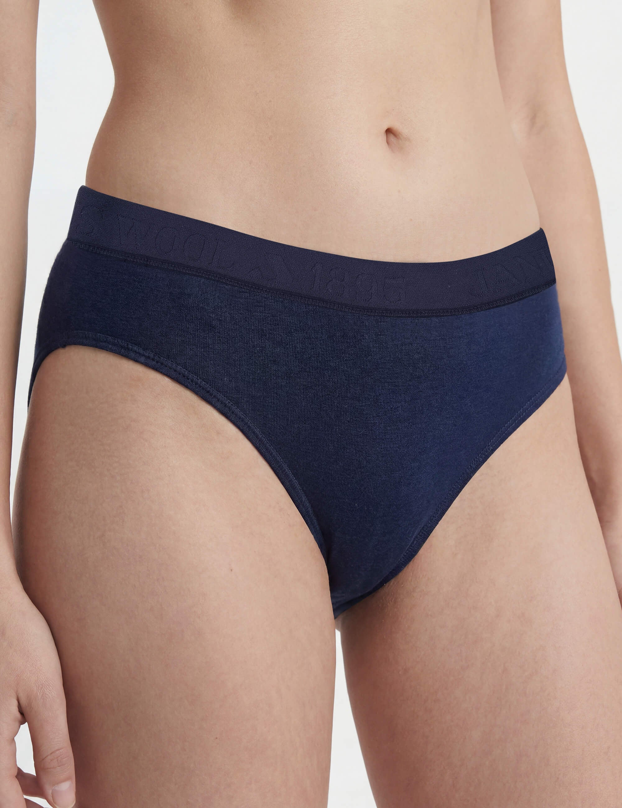 A person wears Briefs – Classic Merino 160 Women in navy blue. These bikini-style, temperature-regulating briefs have a smooth texture and an elastic waistband with subtle embossed text. The photo shows the torso and upper thighs against a plain background.