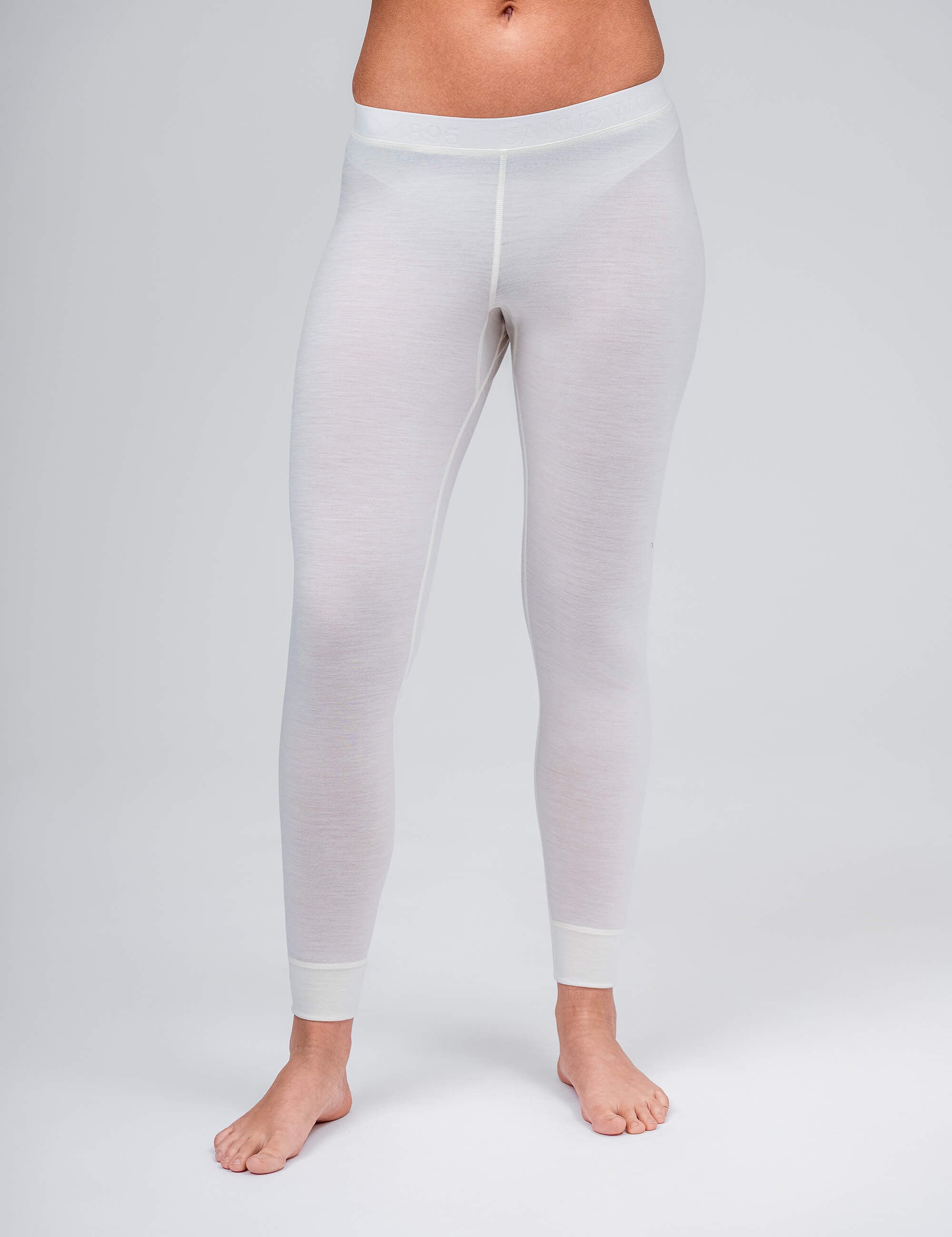 A person is barefoot on a plain light-gray background, wearing Leggings – Classic Merino 160 Women in Marshmallow. The image features the lower torso and legs from the waist down.