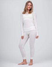 A woman stands barefoot against a light grey background, wearing a matching set featuring the Classic Merino 160 Women leggings, made from lightweight, breathable merino fabric.