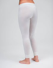 A person stands barefoot on a white background, viewed from the back, wearing Classic Merino 160 Women leggings that are light-colored, semi-sheer, breathable, and temperature regulating.