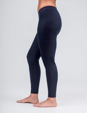 A woman stands barefoot from the waist down, modeling the Classic Merino 160 Women leggings in dark blue against a plain light gray background.