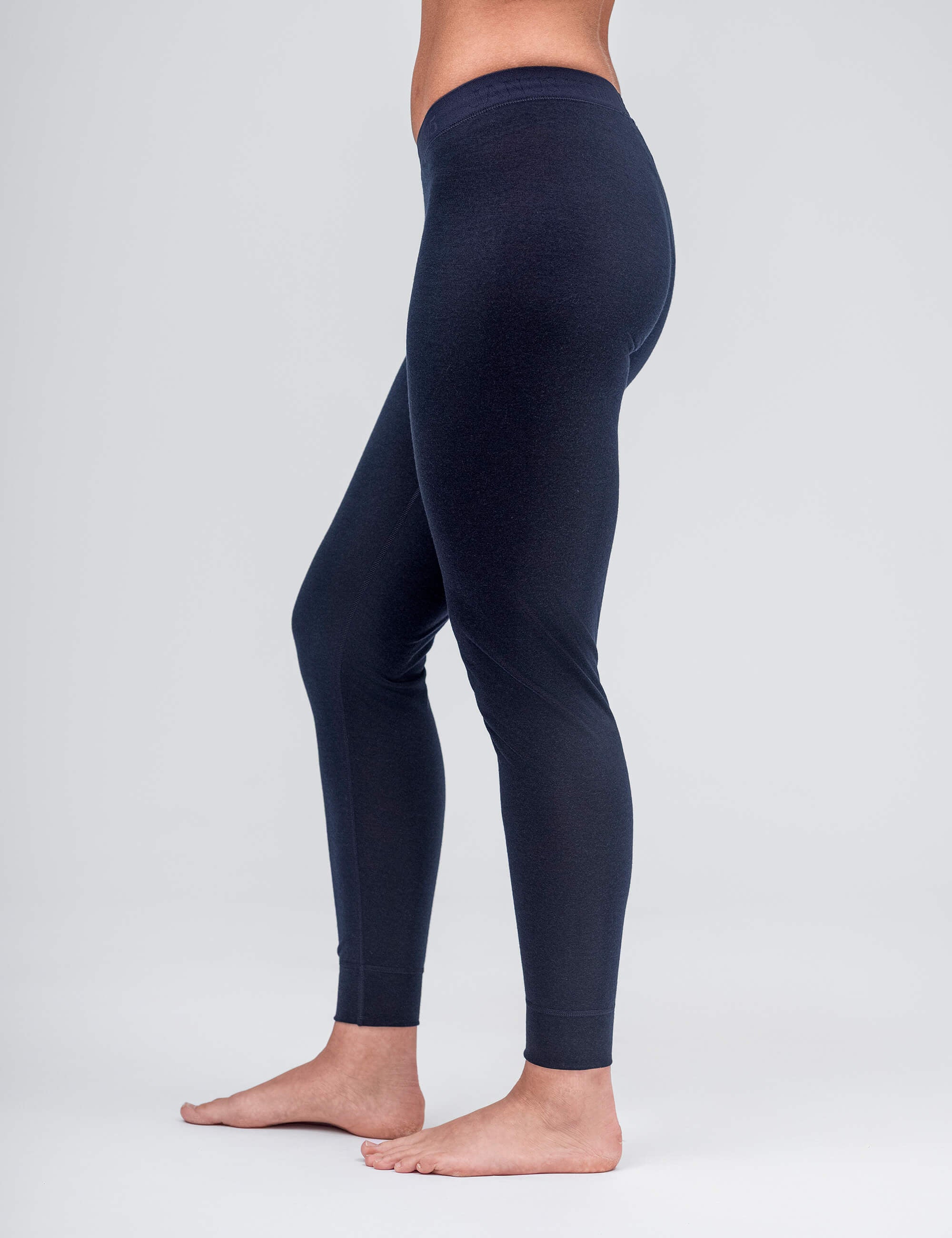 A woman stands barefoot from the waist down, modeling the Classic Merino 160 Women leggings in dark blue against a plain light gray background.