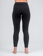 A person stands barefoot, facing away from the camera, wearing Classic Merino 160 Women high-waisted, full-length black leggings against a plain light gray background.