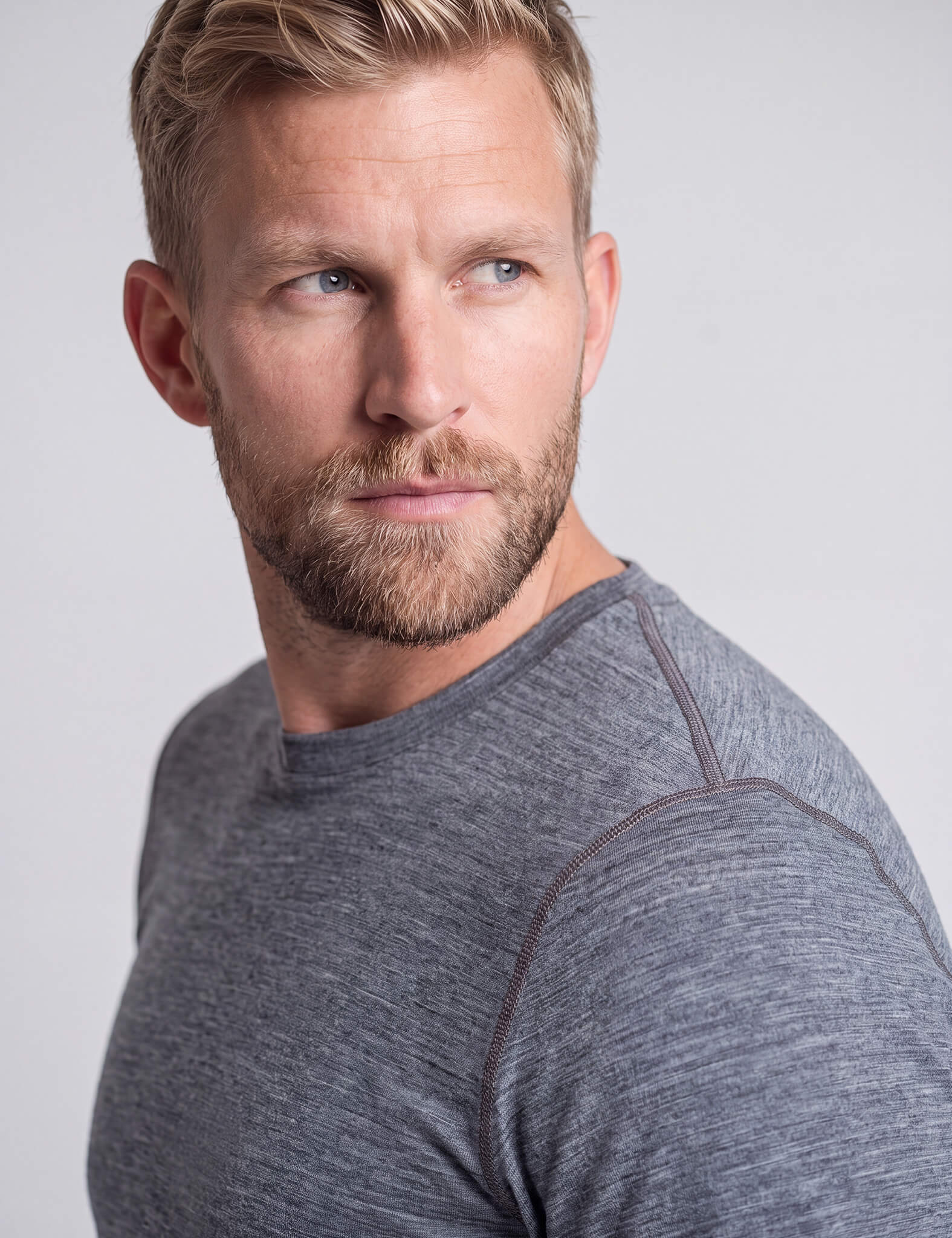 A man with a beard and short, wavy, brown and gray hair wears the T-shirt Active – Classic Merino 160 Men as he looks over his shoulder to the left with a serious expression.