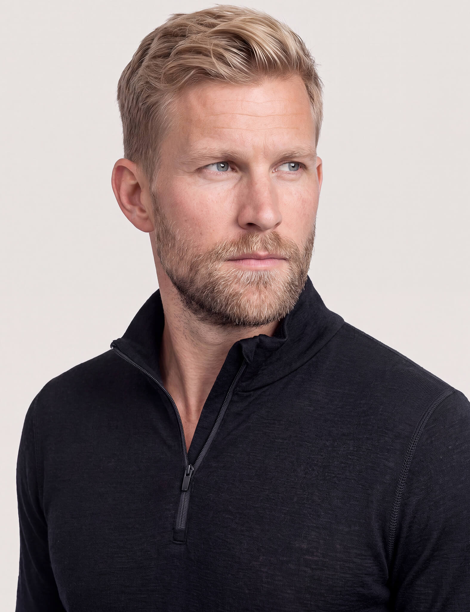 A man with short blond hair and a beard, wearing the Half Zip – Classic Merino 160 Men in black, looks slightly to the left against a plain light background.