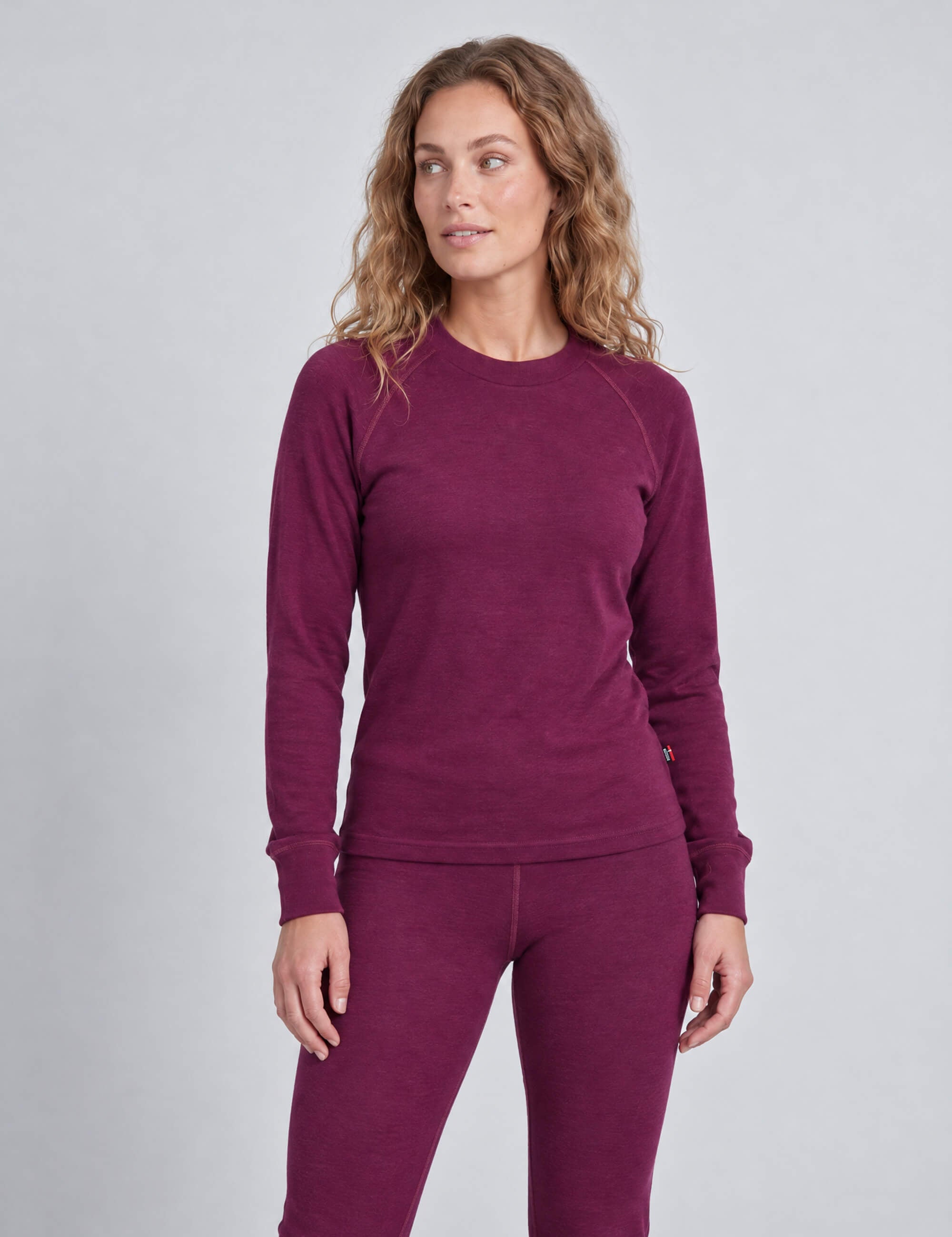 A woman wearing a purple Wool Set – Classic Merino 200 Rib Women featuring a long-sleeved crewneck top and matching leggings.
