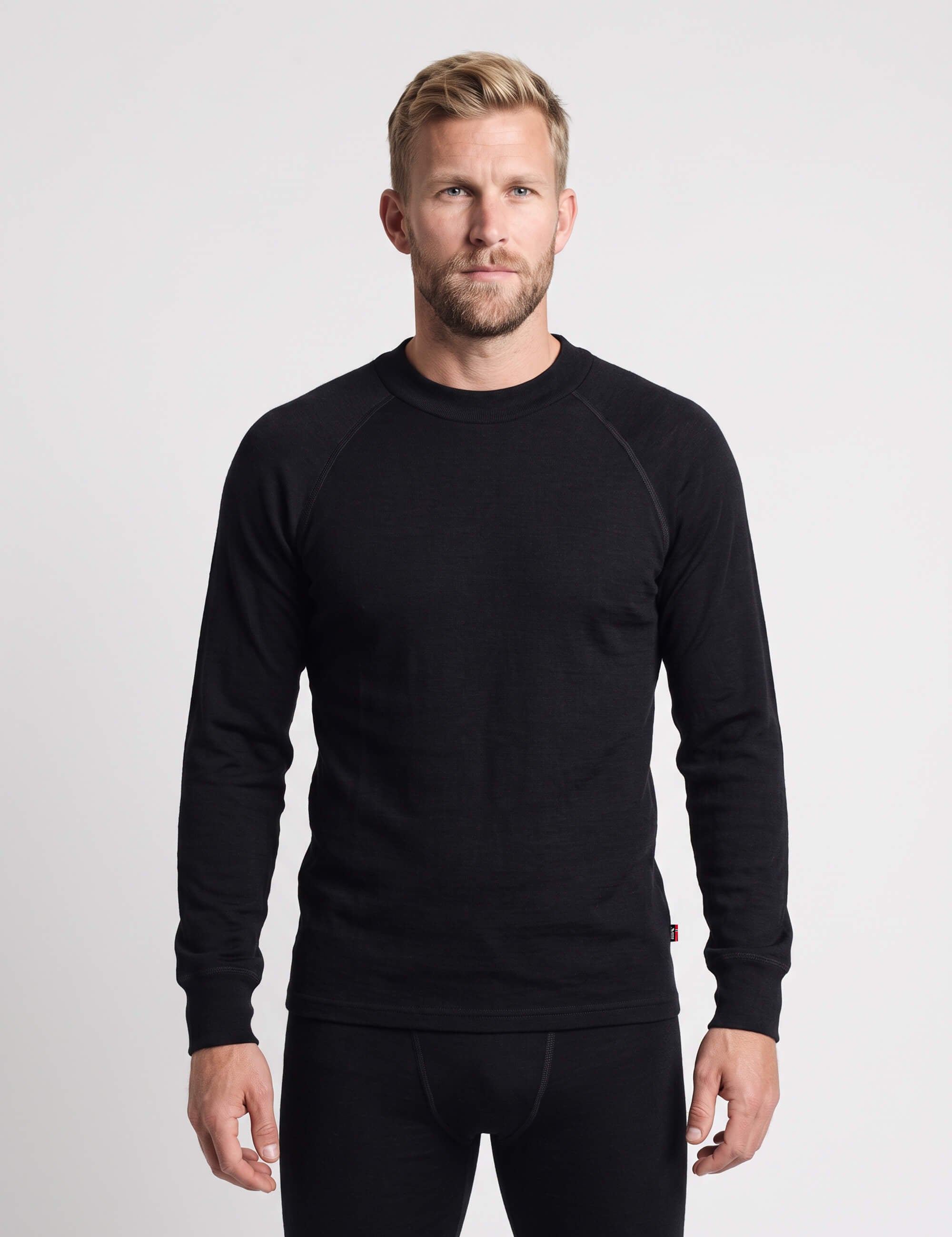 A man wearing a black Wool Set – Classic Merino 200 Rib Men long-sleeved crew-neck shirt and matching base layer bottoms.