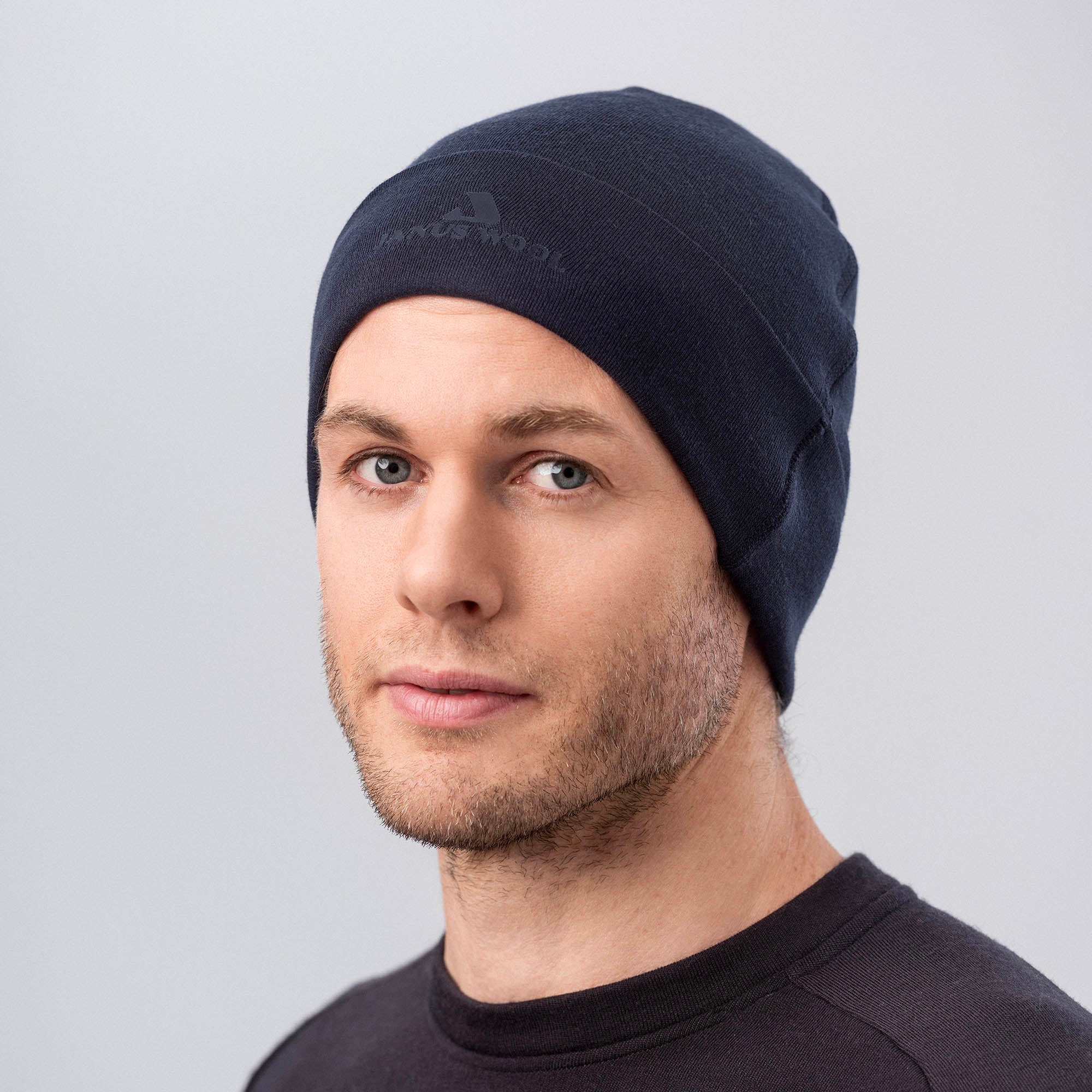 A man with light skin, blue eyes, and short brown facial hair wears the Classic Merino 215 Beanie in dark navy with a matching shirt, looking slightly to the side against a light gray background for style and breathability.