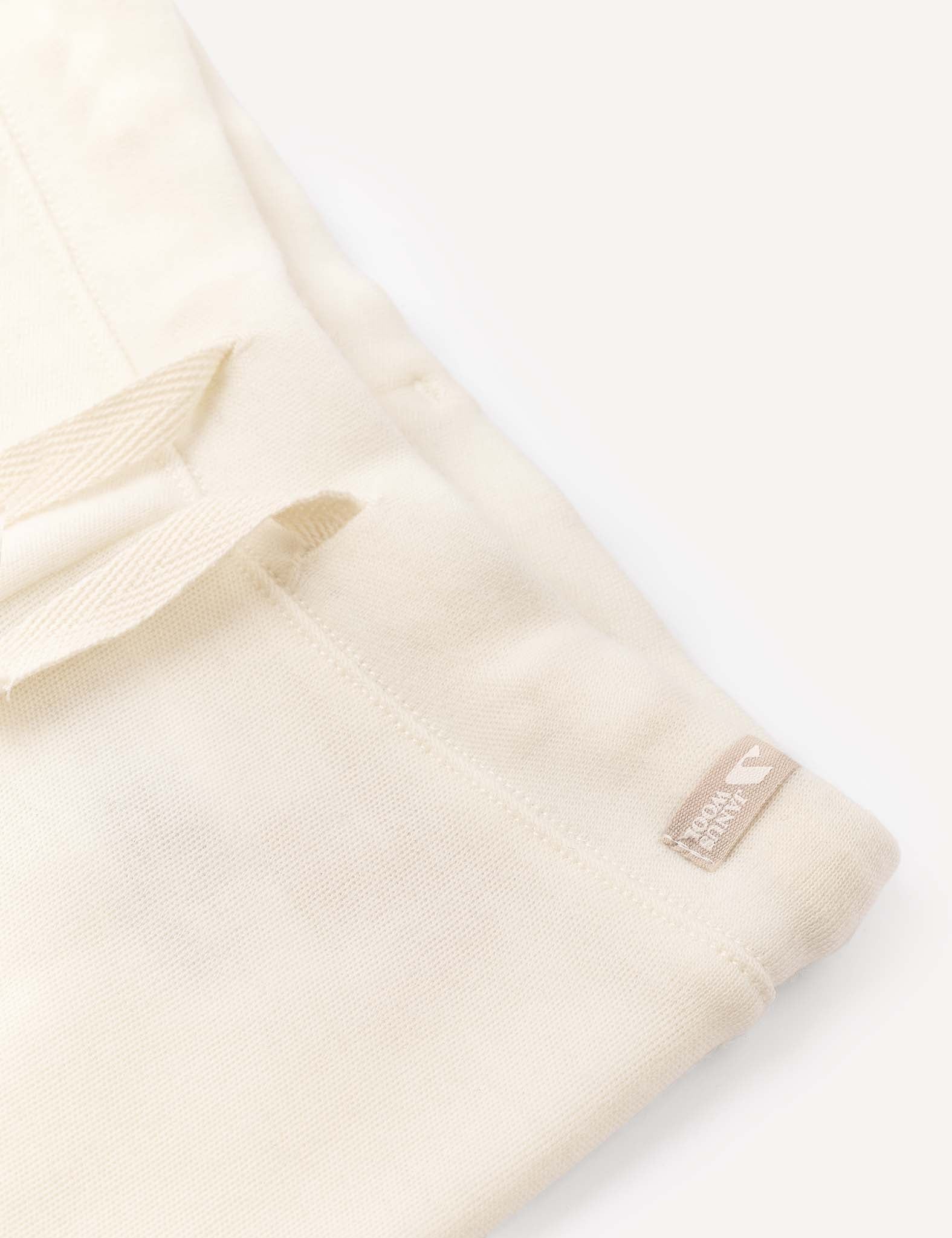 Soft cream-colored AirWool pants featuring a visible textured finish, drawstring loops, and a small sewn label displaying “100% ORGANIC COTTON” alongside a heart icon. These relaxed-fit Pants – Merino Baby AirWool are styled against a light, neutral background.
